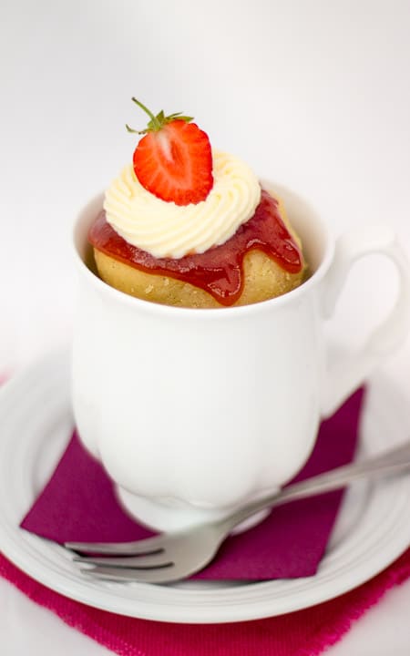 Strawberries and cream cake in a mug topped with icing and a strawberry