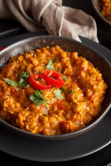 Lentil dahl in a black bowl topped with coriander and red chilli