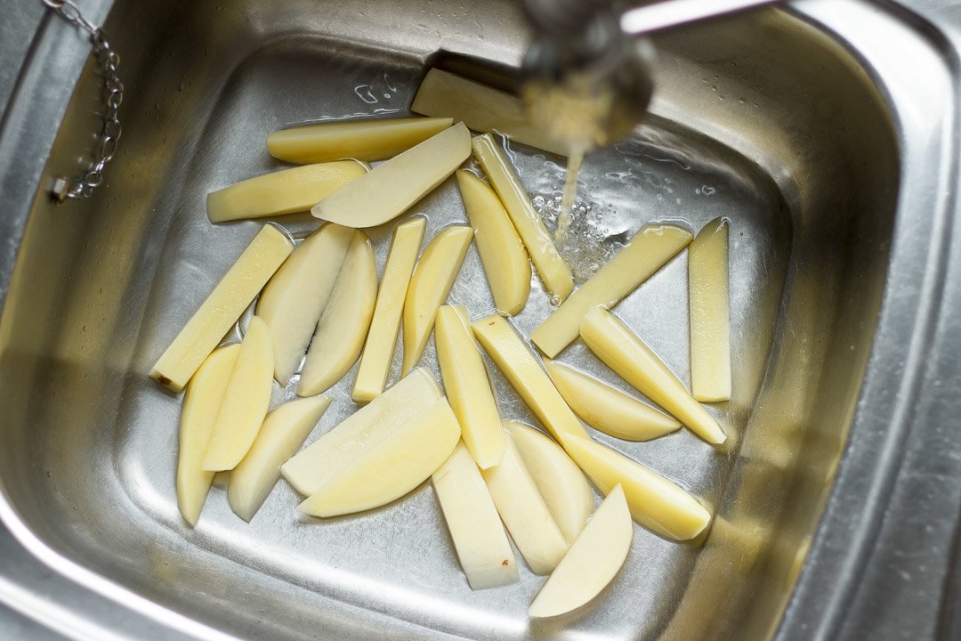 cut potato wedges in a sink being rinsed with water