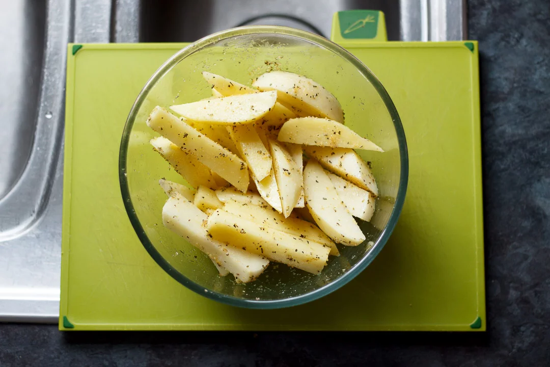 cut washed and dried potato wedges in a glass bowl with herbs and oil mixed through