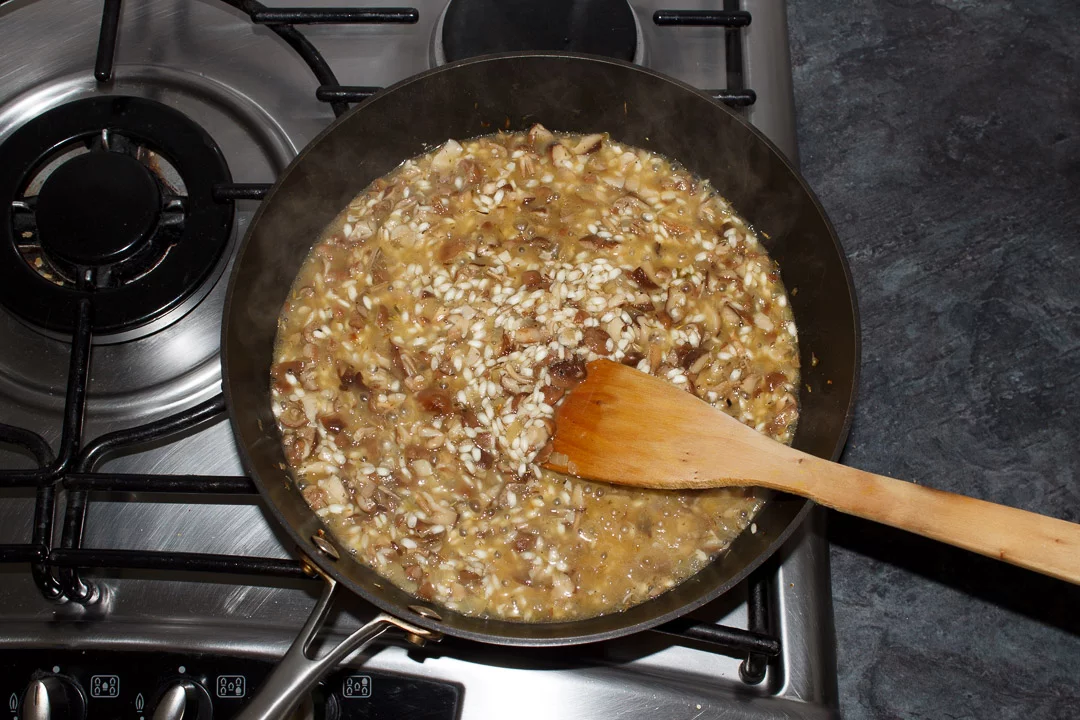 wild mushroom risotto in a large saucepan with stock beginning to be added to it