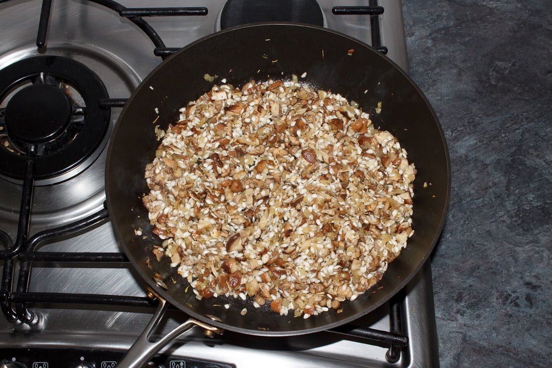 onion, garlic and mushrooms frying in a large saute pan with added arborio rice