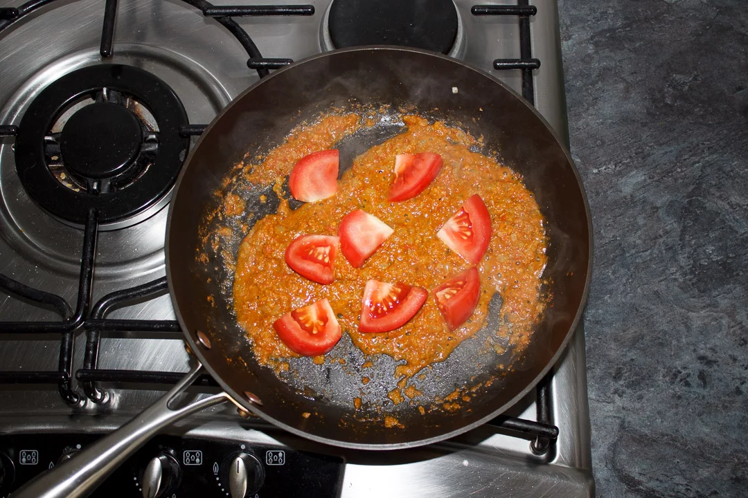 bombay aloo sauce mixture in a large saute pan with tomato wedges