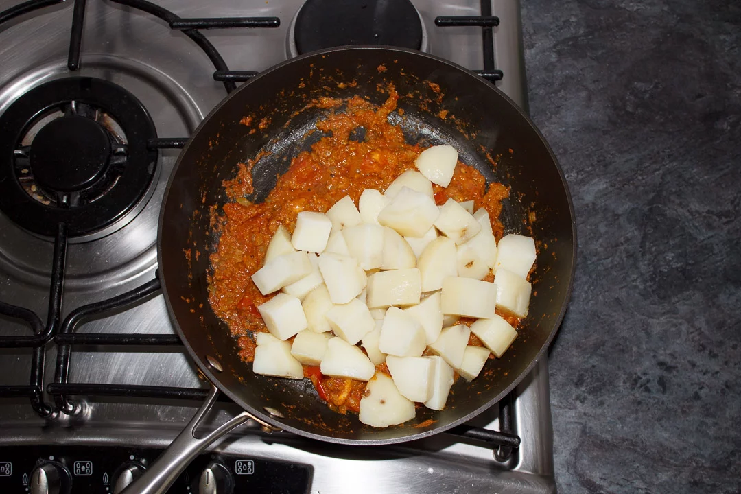 Cooked, cubed potatoes in a large saute pan with bombay aloo sauce