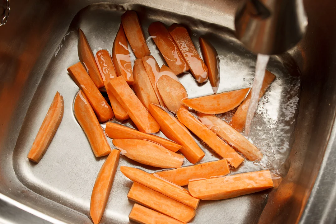 sweet potato wedges being rinsed in cold water