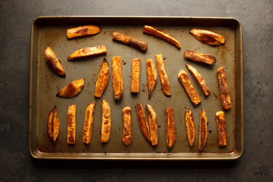 cooked sweet potato wedges spaced out on a baking tray