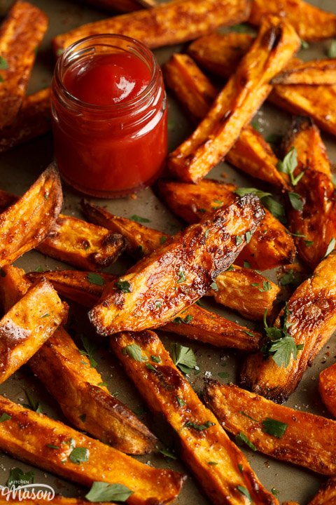 Baked sweet potato wedges on a baking tray with tomato sauce