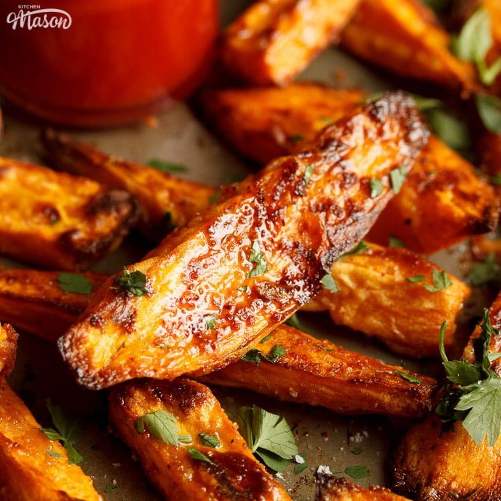Baked sweet potato wedges on a baking tray with tomato sauce
