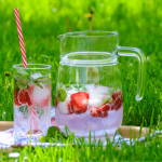 A jug and glass filled with strawberry infused water on a tray in a field