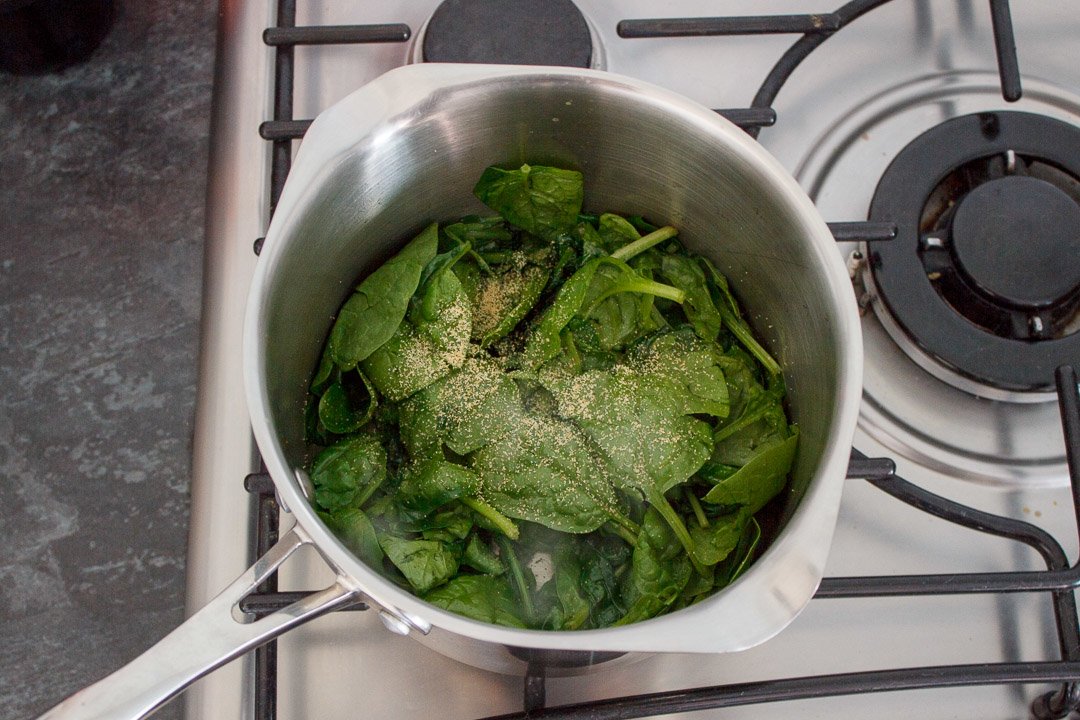 wilted spinach in a saucepan with garlic powder and salt