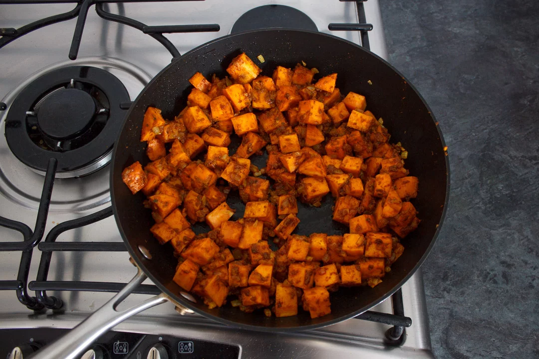 Sweet potato, onion and curry paste frying in a frying pan