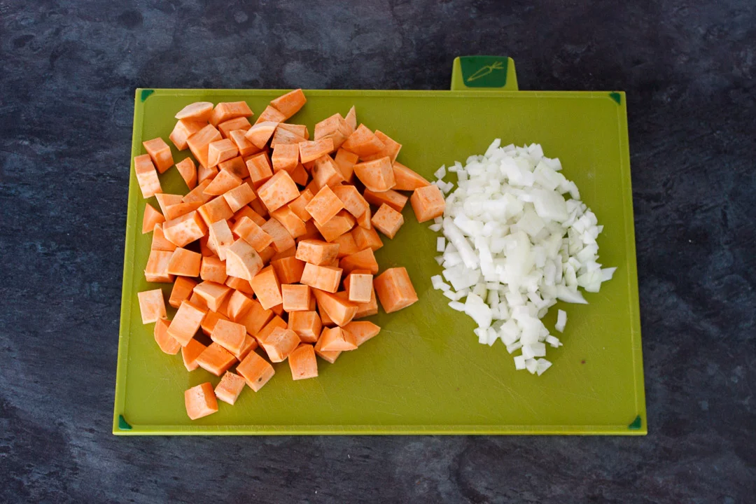cubed sweet potato and diced onion on a green chopping board
