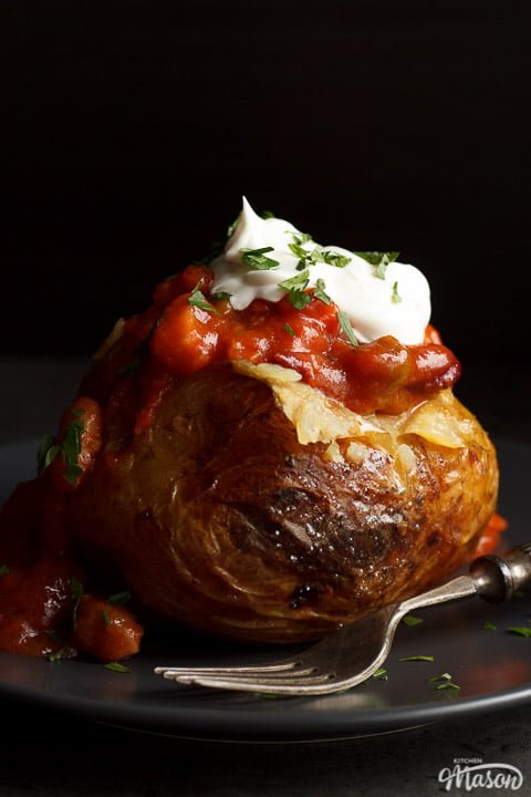 A slow cooker jacket potato on a grey plate topped with vegan chilli and vegan creme fraiche
