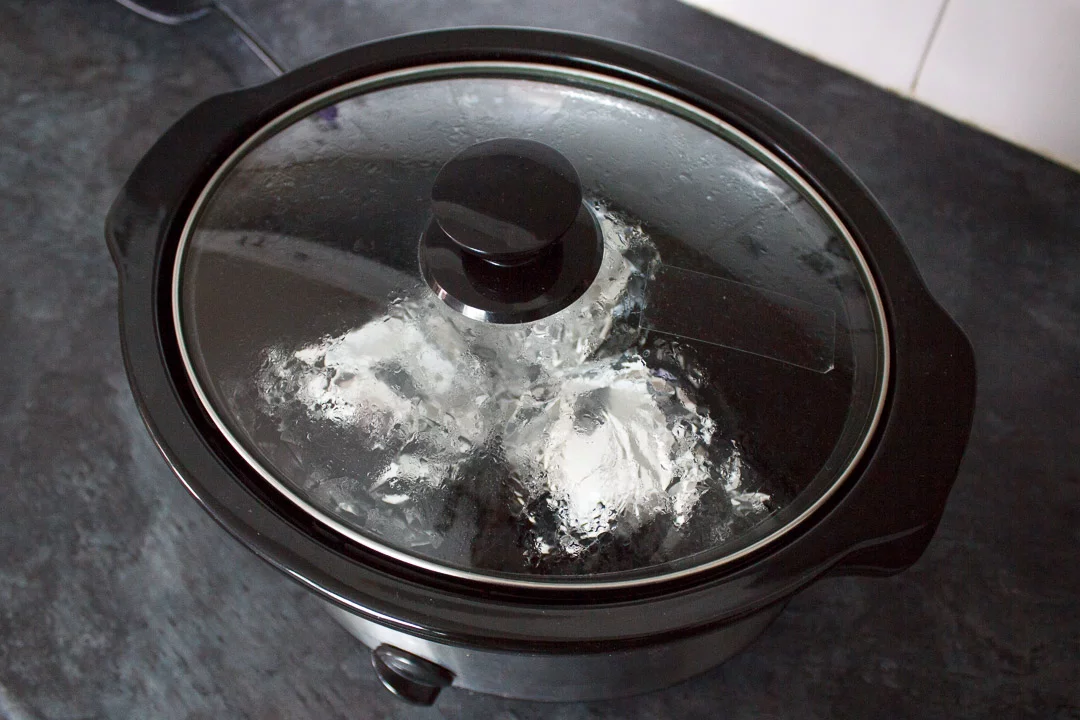 jacket potatoes wrapped in foil, cooking in a slow cooker