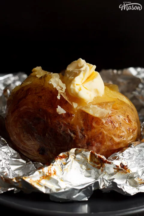 A slow cooker jacket potato on foil topped with melting vegan butter