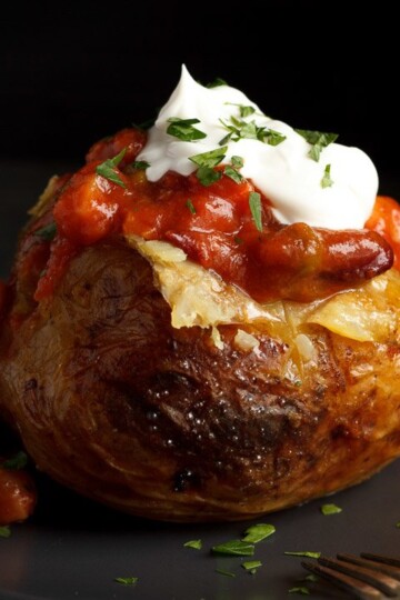 A slow cooker jacket potato on a grey plate topped with vegan chilli and vegan creme fraiche