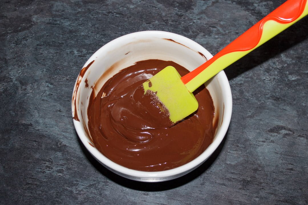 melted dark chocolate in a white bowl with a green spatula