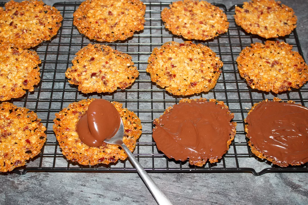 Florentine cookies on a cooling rack with dark chocolate being spread on them