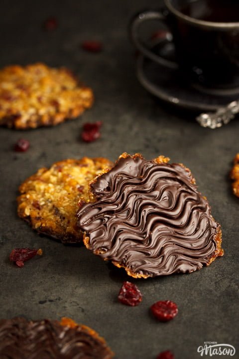 Chocolate florentines on a worktop with dried cranberries scattered around them