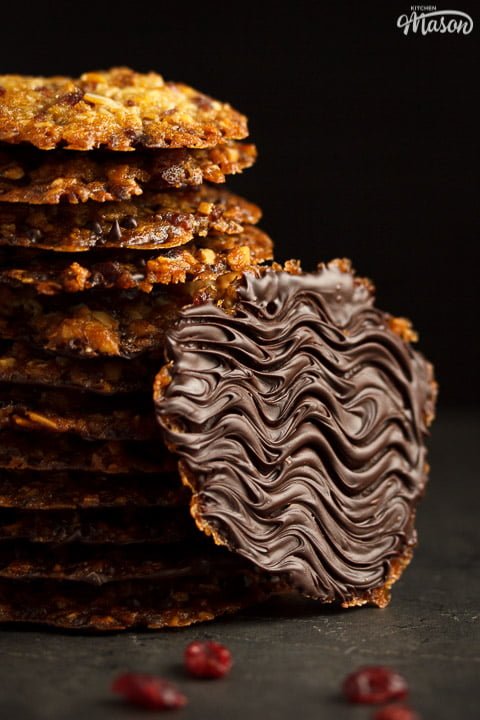 Chocolate florentines in a stack with dried cranberries scattered around them