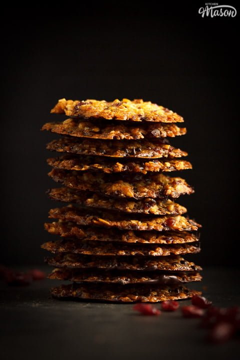Chocolate florentines in a stack with dried cranberries scattered around them