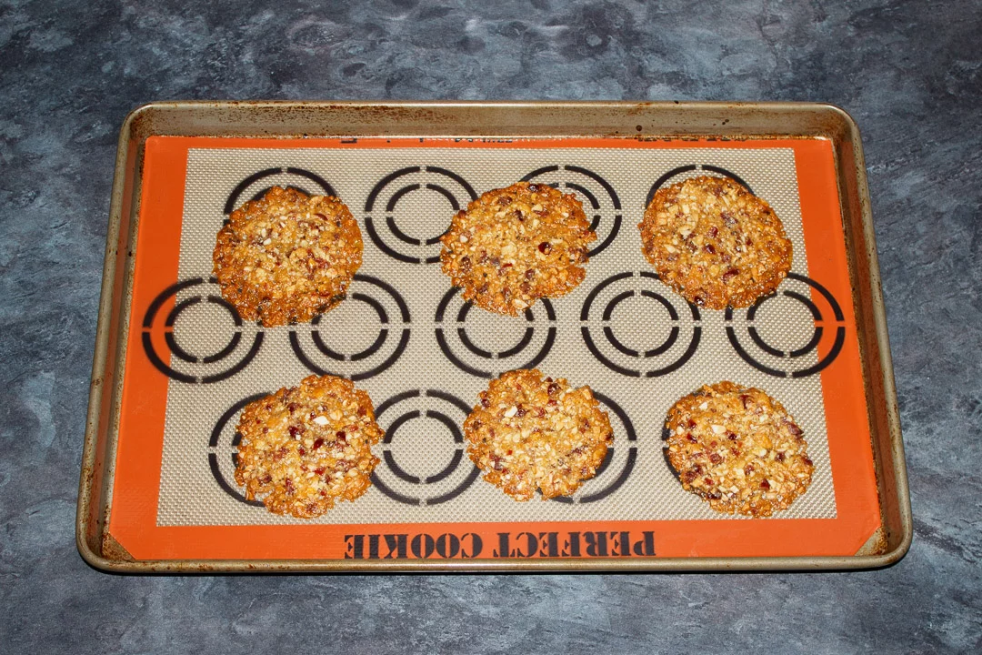 Baked florentine cookies spaced out on a large baking tray lined with a silicone mat