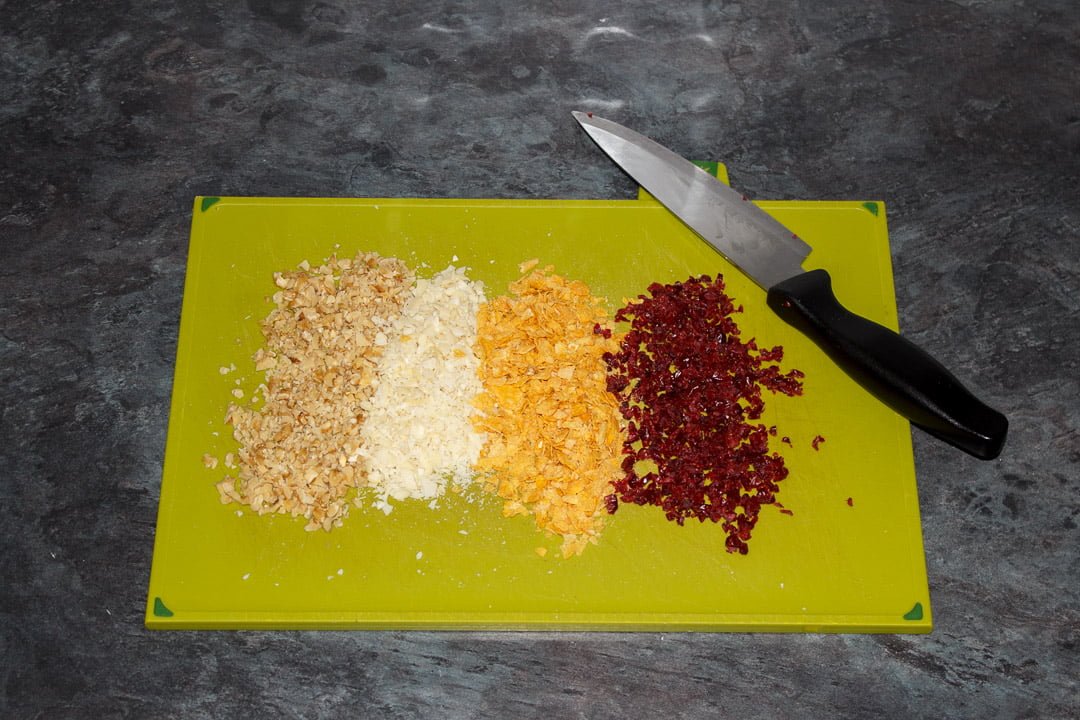 finely chopped nuts, cranberries and cornflakes on a green chopping board