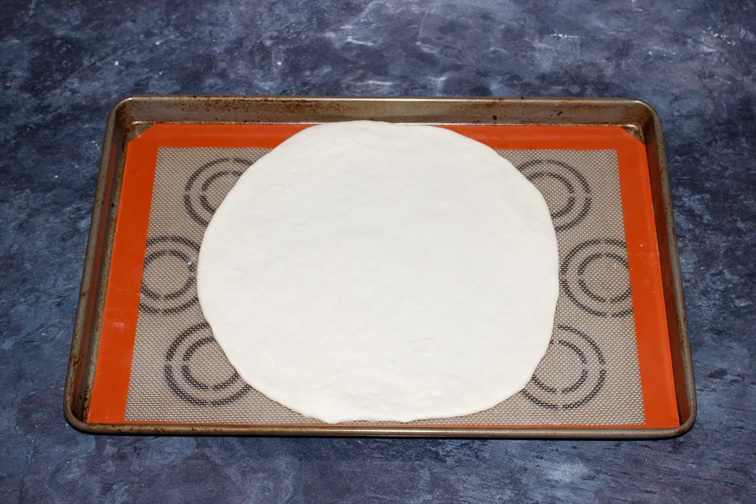 Round pizza dough on a large baking tray lined with a silicone mat