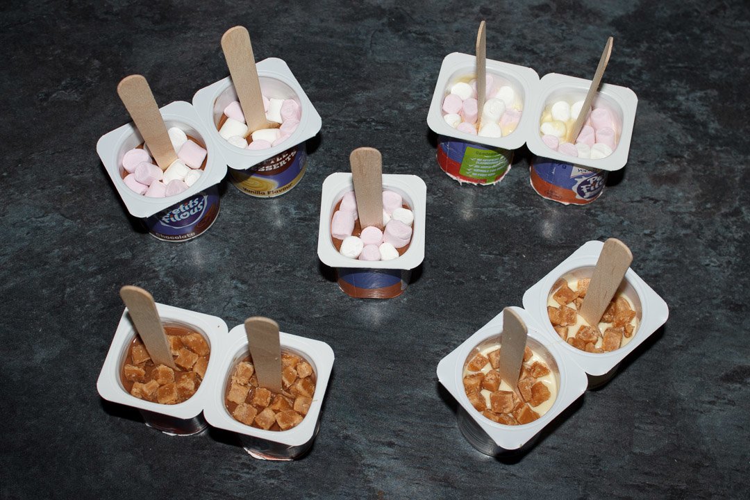 Hot chocolate sticks topped with mini marshmallows and fudge pieces, ready to be put in the fridge to set
