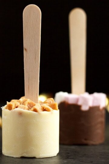 Hot chocolate sticks topped with fudge pieces and marshmallows surrounded by gold curling ribbon