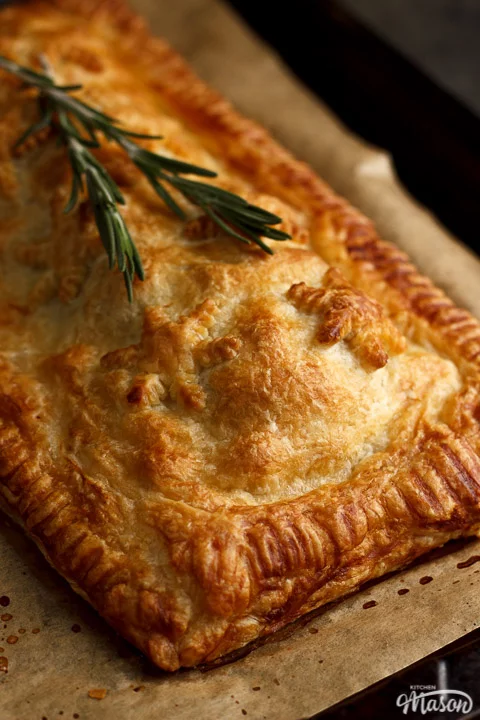 A Baked, golden vegetable wellington on a lined baking tray topped with rosemary sprigs