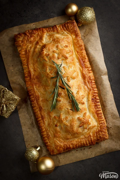A Baked, golden vegetable wellington on a lined baking tray topped with rosemary sprigs