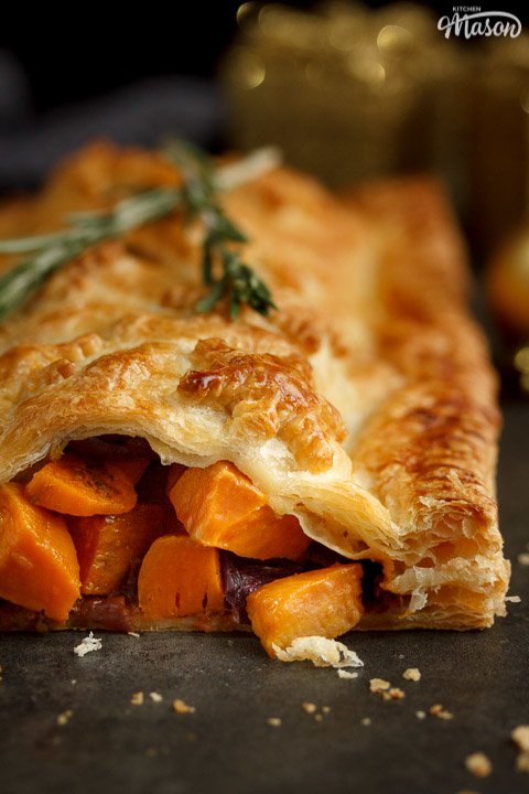 Sweet potato cubes and red onion falling out of a vegetable wellington topped with rosemary sprigs