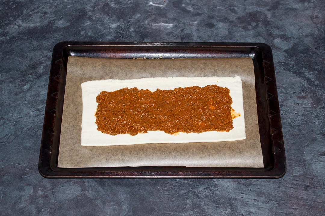 A rectangle of puff pastry on a lined baking tray topped with red pesto