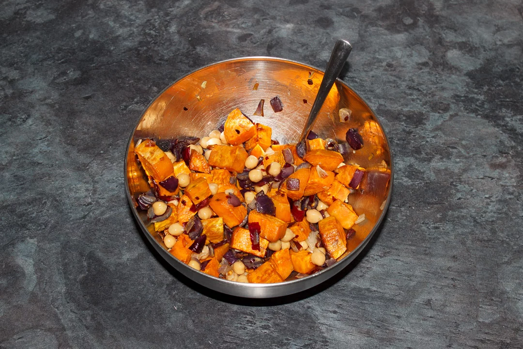 Chickpeas, roasted sweet potatoes, red onion and garlic mixed together in a metal bowl