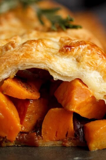 Sweet potato cubes and red onion falling out of a vegetable wellington topped with rosemary sprigs