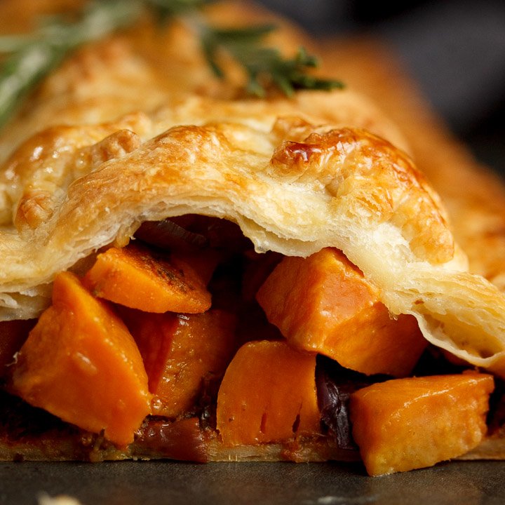 Sweet potato cubes and red onion falling out of a vegetable wellington topped with rosemary sprigs