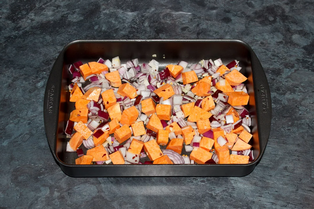 Sweet potato. red onion and garlic coated in oil and salt in a roasting tray