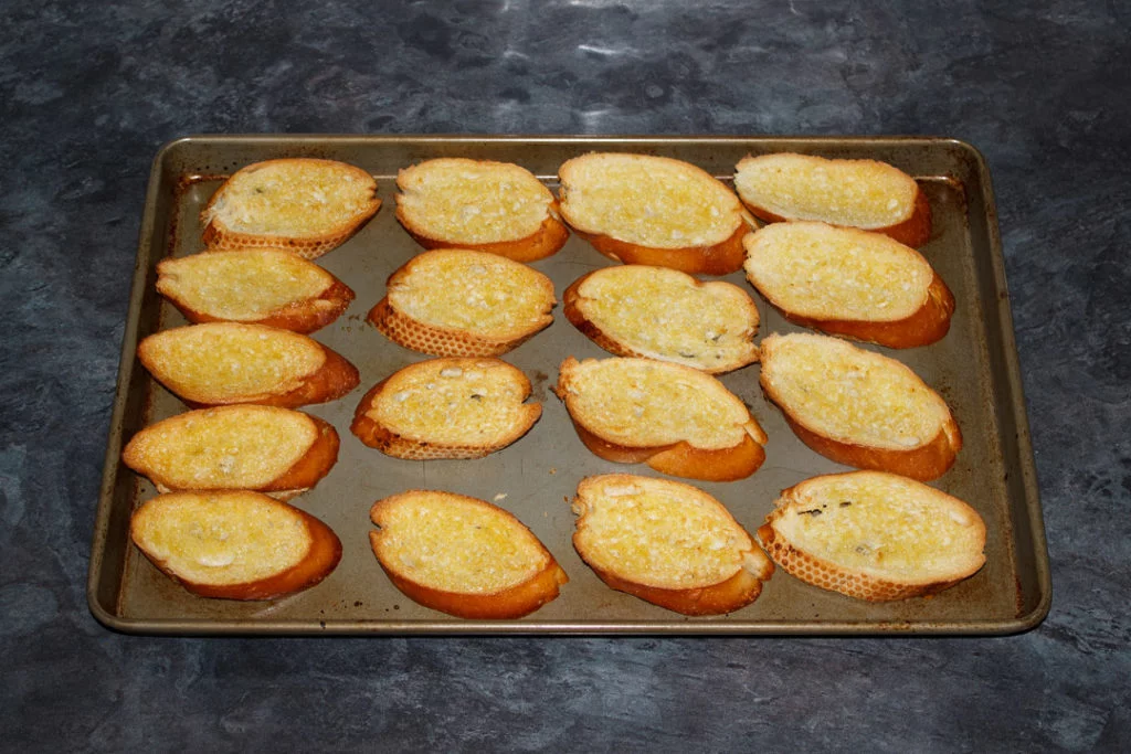 Cooked, crispy and golden baguette slices on a large baking sheet.