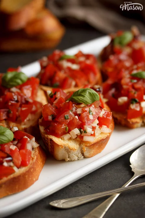 bruschetta topped with a basil leaf on a white serving plate