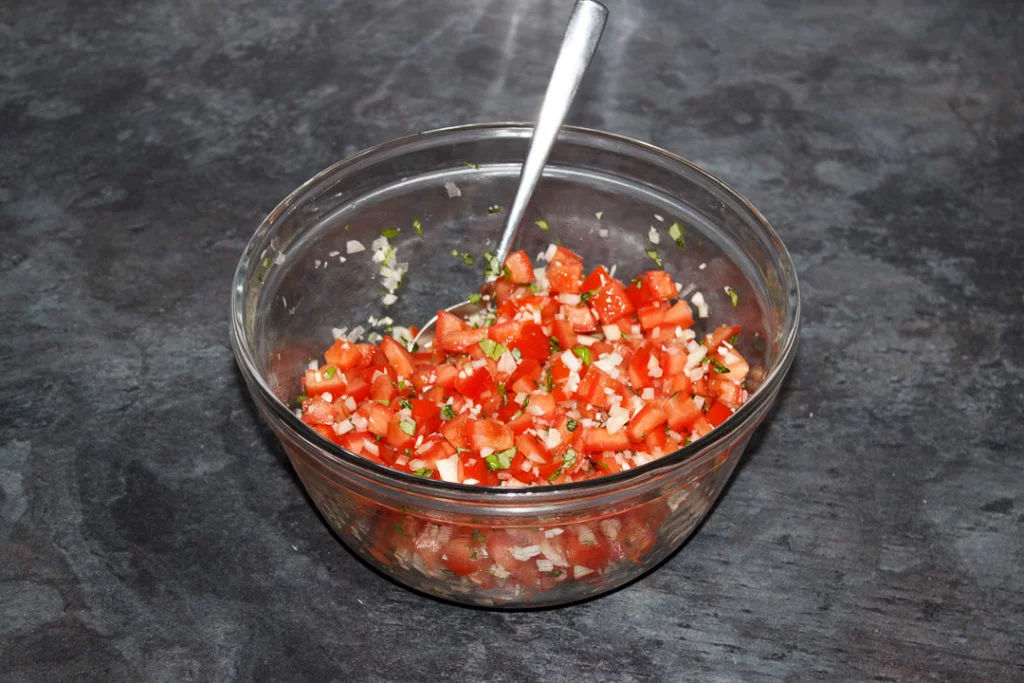 Bruschetta topping in a large glass bowl with a spoon.