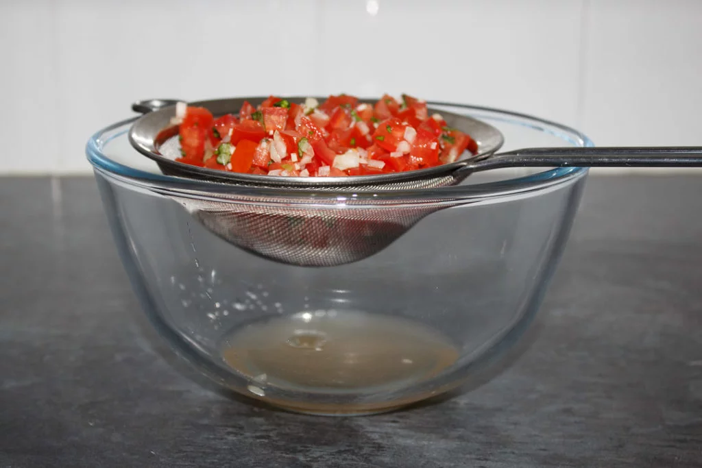 Bruschetta topping in a seive, draining over a large bowl.