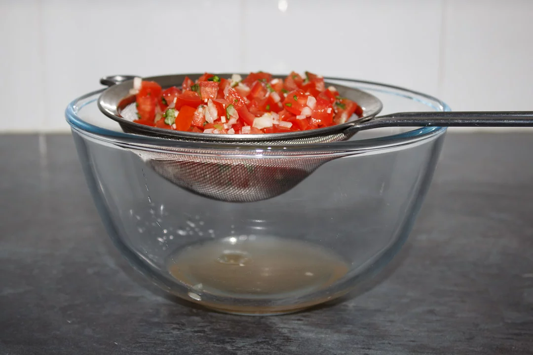 Bruschetta topping in a seive, draining over a large bowl
