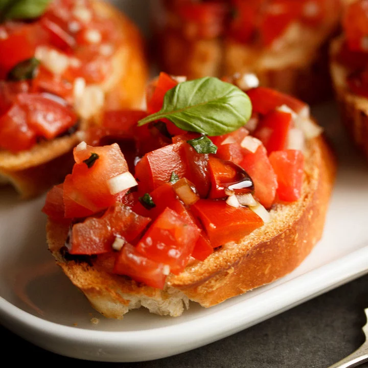 bruschetta topped with a basil leaf on a white serving plate