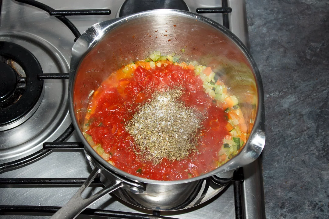 Vegetables, tinned tomatoes and herbs cooking in a large saucepan