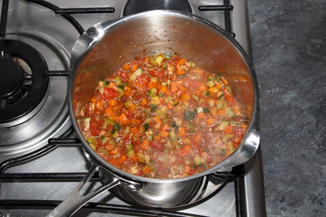Vegetables, tinned tomatoes and herbs cooking in a large saucepan