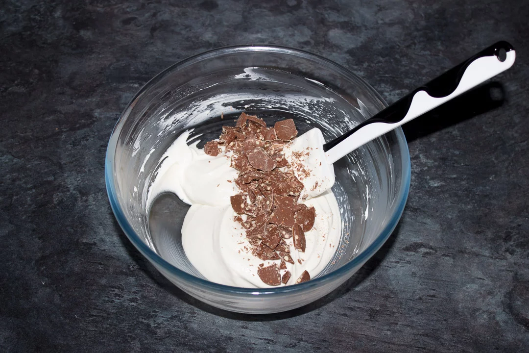 Chopped Malteser Buttons on top of a cheesecake filling mixture in a glass bowl with a white spatula