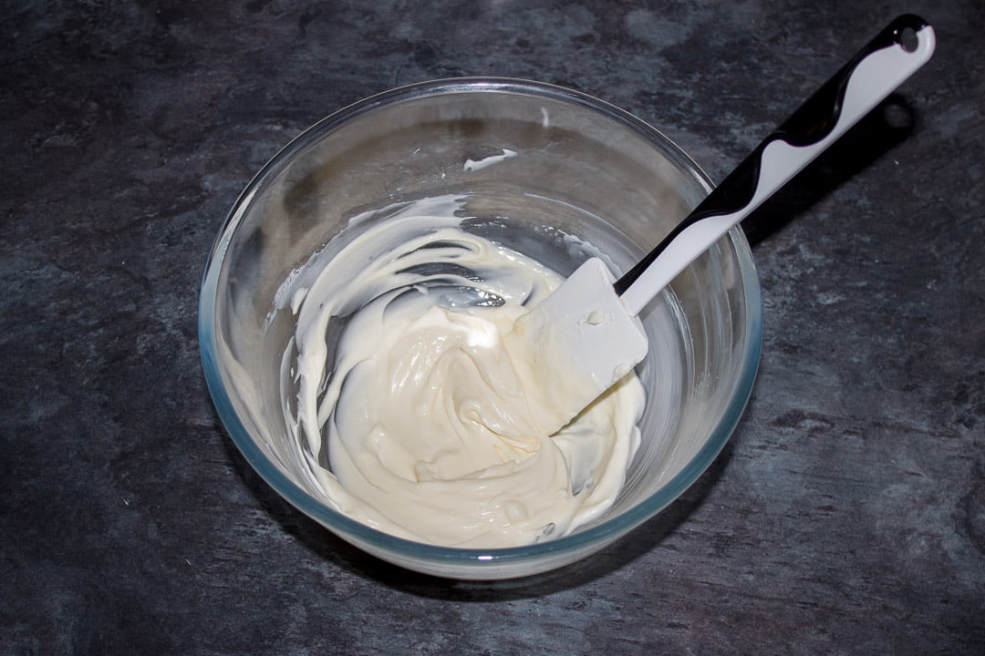 Cream cheese, vanilla and icing sugar mixed together in a glass bowl with a white spatula