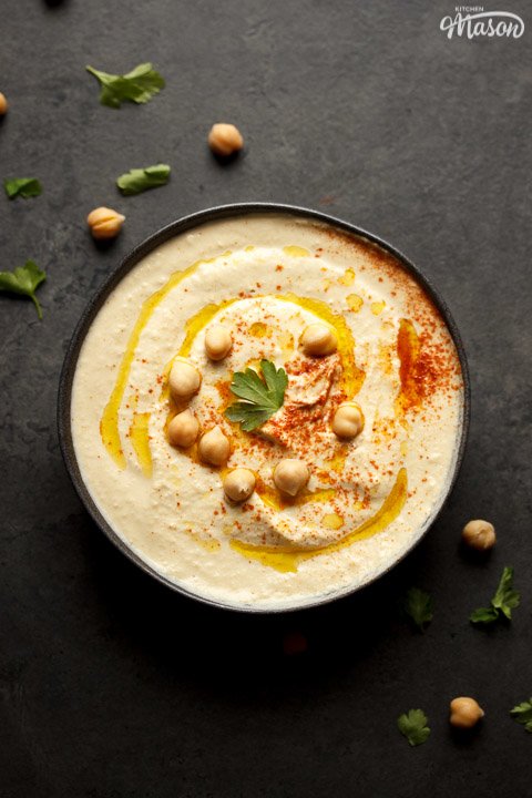Homemade hummus in a bowl topped with chickpeas, olive oil, paprika and parsley