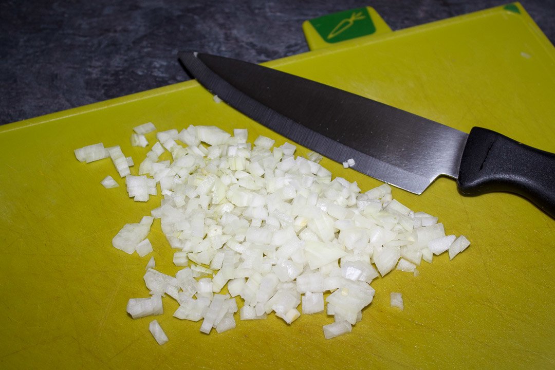 Diced onion on a green chopping board with a sharp knife